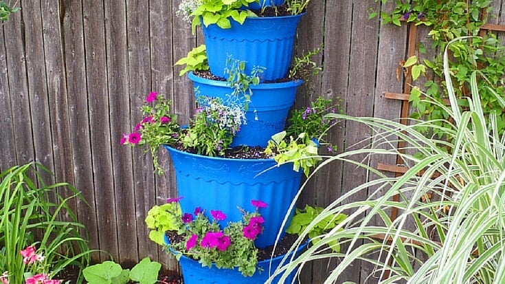 Plastic planters stacked from largest to smallest, leaned up against a wooden fence, being used for container planting.