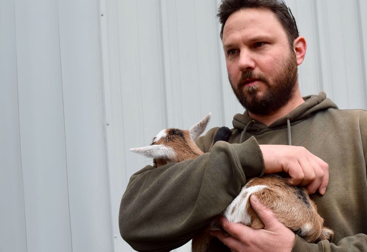 Michael holding a Nigerian Dwarf goat kid, showing the gentle care given to animals on the farm.