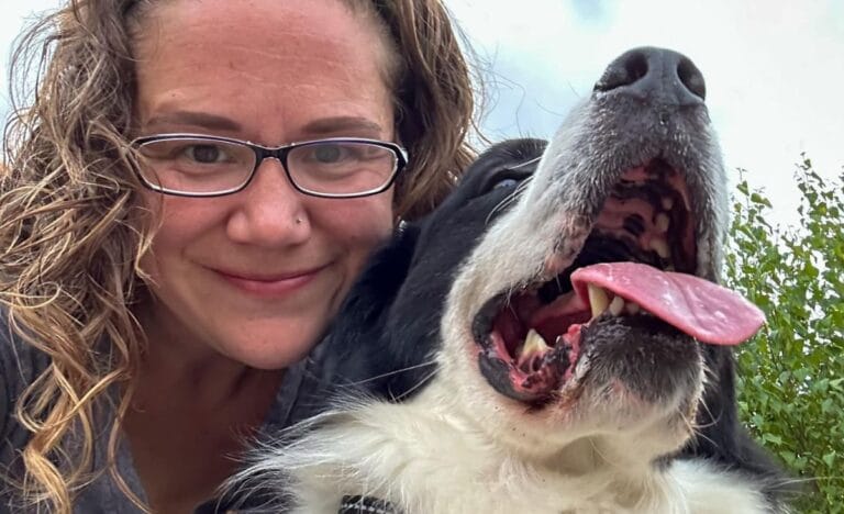 Jessica Knowles smiling with her black and white dog on her homestead, showcasing the joy of farm life.