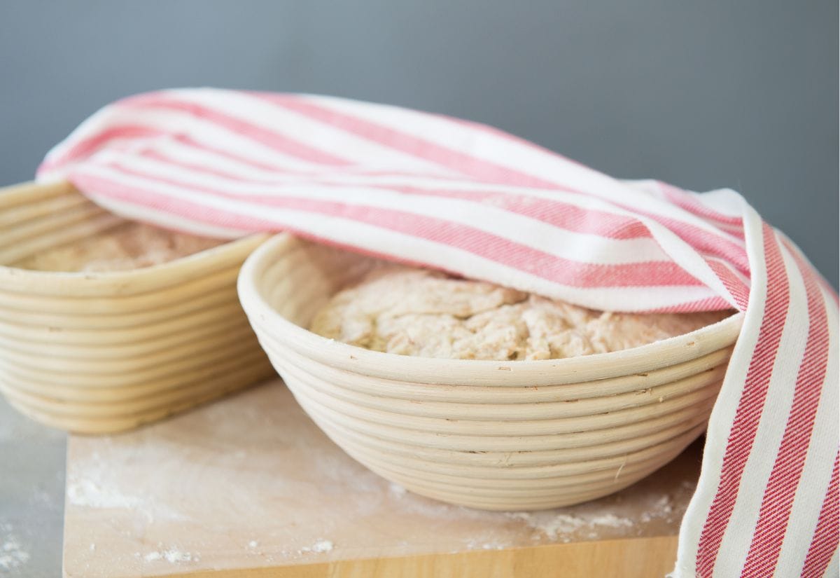 Bread dough rising in a banneton basket, covered with a striped cloth.