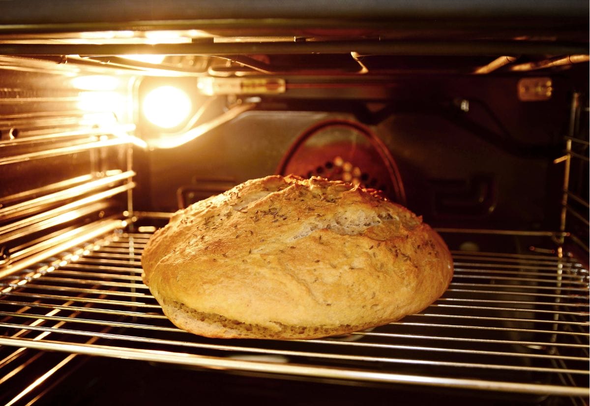 A golden-brown loaf of bread baking in the oven with a light on.