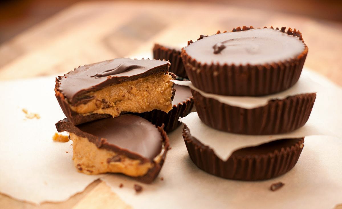 Homemade peanut butter cups stacked on parchment paper, one cut open to reveal the rich, soft peanut butter center beneath glossy chocolate.