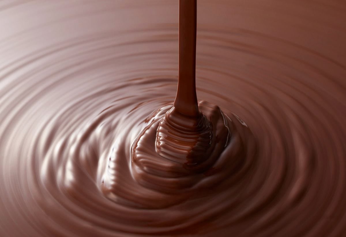 Melted milk chocolate being poured, creating glossy ripples perfect for layering in homemade peanut butter cups.