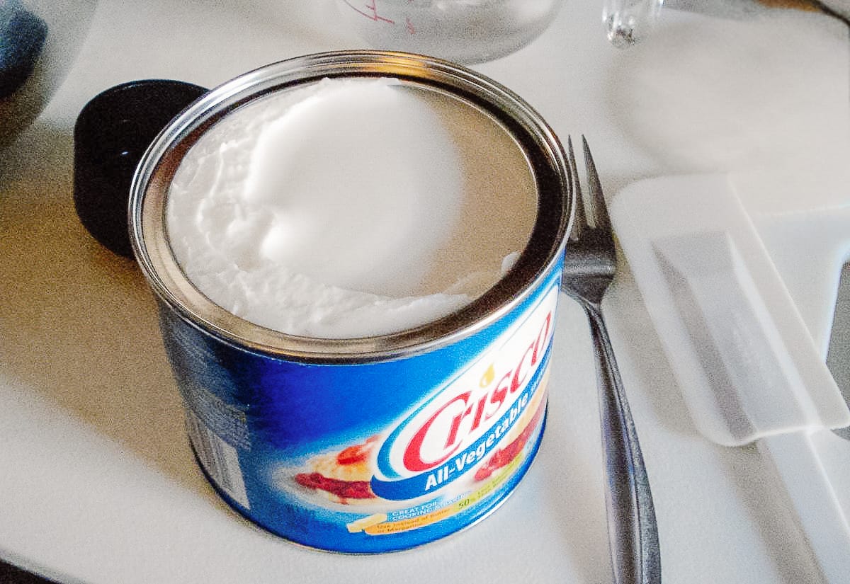 An open can of Crisco all-vegetable shortening with a spatula beside it, showing the ingredient used to make smooth, easy-to-bite chocolate.