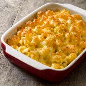 Golden and bubbly baked macaroni and cheese in a red and white ceramic baking dish on a rustic wooden surface.