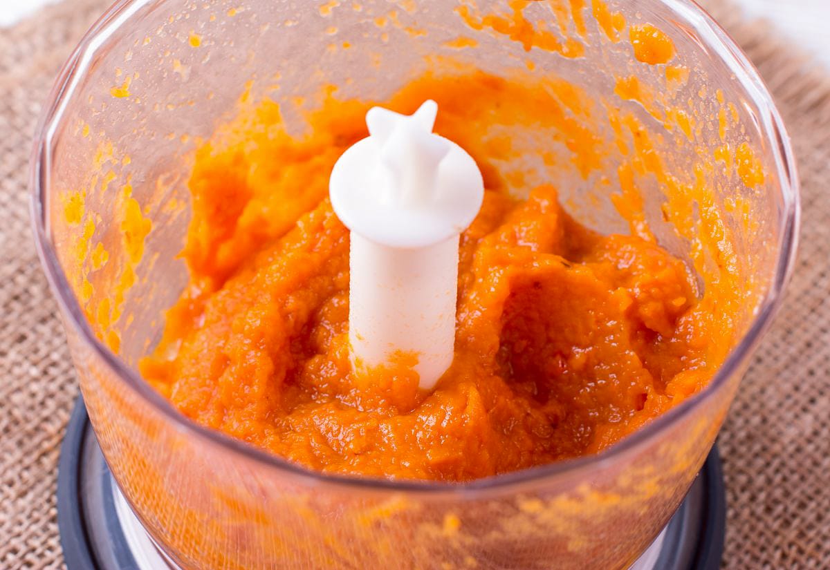 Bright orange homemade pumpkin puree inside a food processor bowl, showing the thick, smooth consistency after blending.