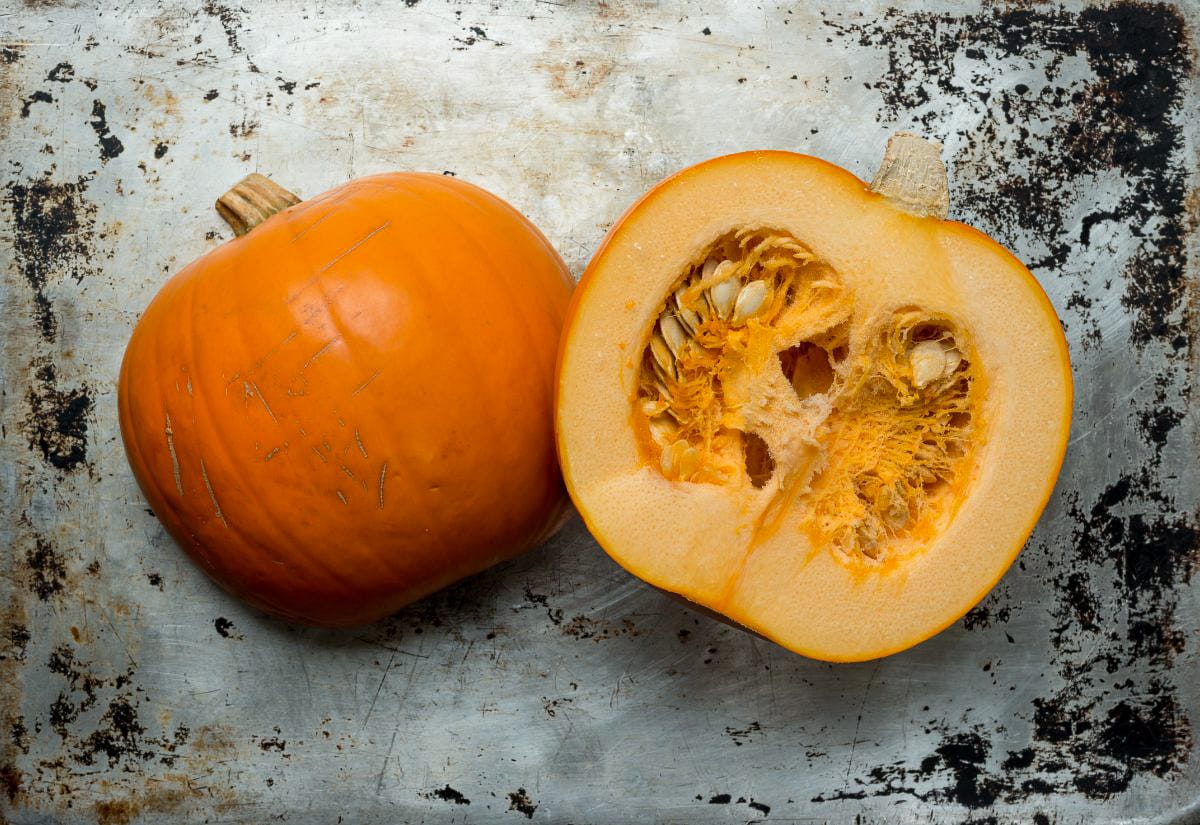 A freshly cut sugar pumpkin resting on a worn metal baking sheet, showing the firm orange flesh and seed cavity before roasting.