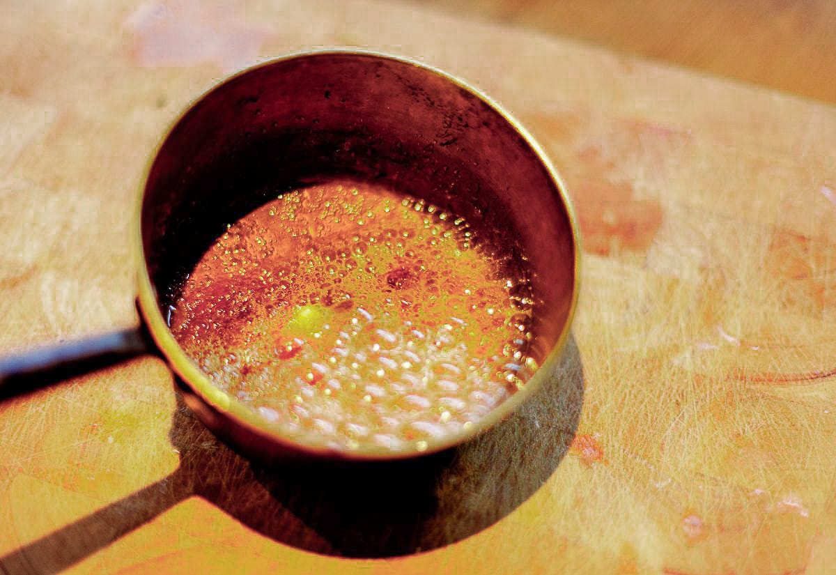 A small saucepan filled with bubbling hot caramel on a wooden cutting board, ready to become the base for homemade butterbeer.