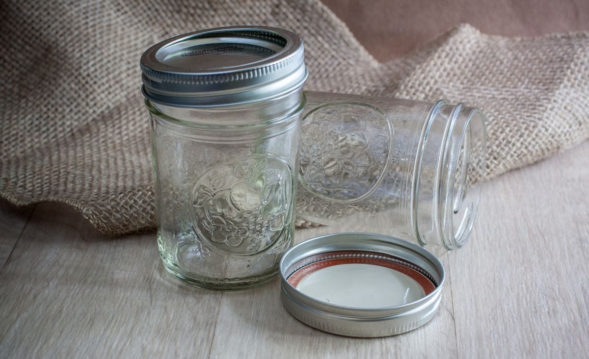 Two empty jelly-sized mason jars sitting on a counter with burlap in the background.