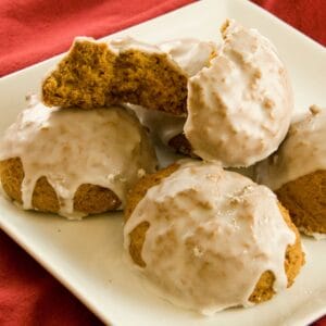 A close-up of chewy pumpkin cookies with maple icing, served on a white plate with a vibrant red background.