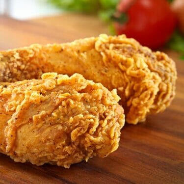 A closeup of fried chicken on a wooden cutting board.