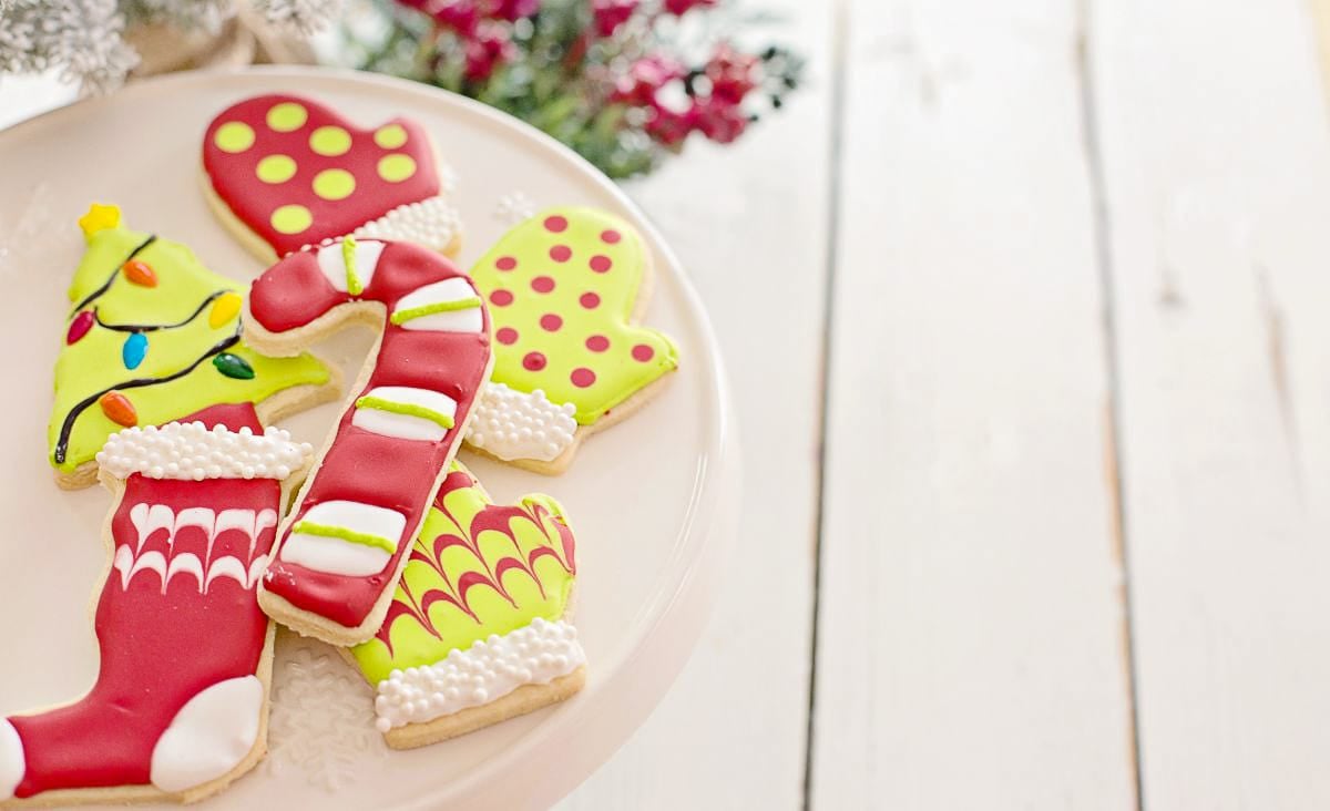 A plate of brightly decorated holiday sugar cookies, including mittens, stockings, and a candy cane, all colored with vivid natural icing.