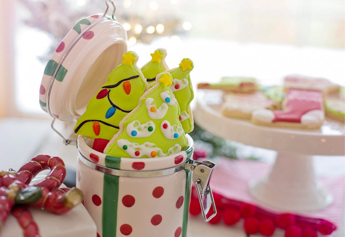 Lime-green Christmas tree sugar cookies standing in a red-and-white holiday tin, decorated with natural food coloring and surrounded by a soft, festive background.