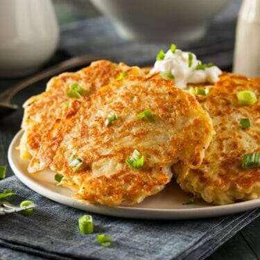 Potato pancakes on a plate with sour cream and slices of green onion.