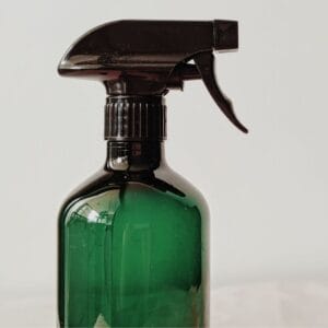 A green glass spray bottle of homemade teat wash.