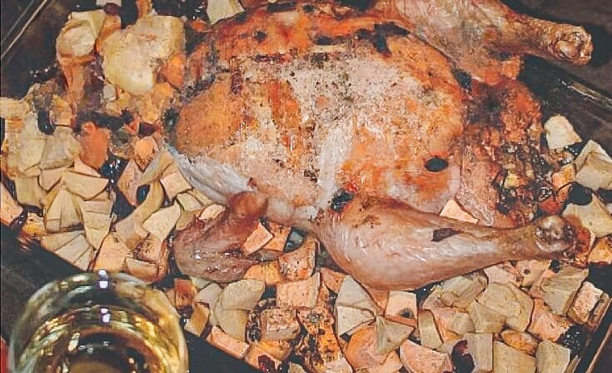 Close-up of a roasted whole chicken sitting on top of a layer of sweet potato, apple, and cranberry stuffing, showing the caramelized skin and rustic pan juices.