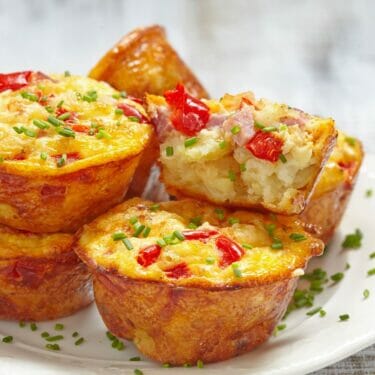A white plate with red pepper, cheddar, and ham mini quiches topped with chopped chives.