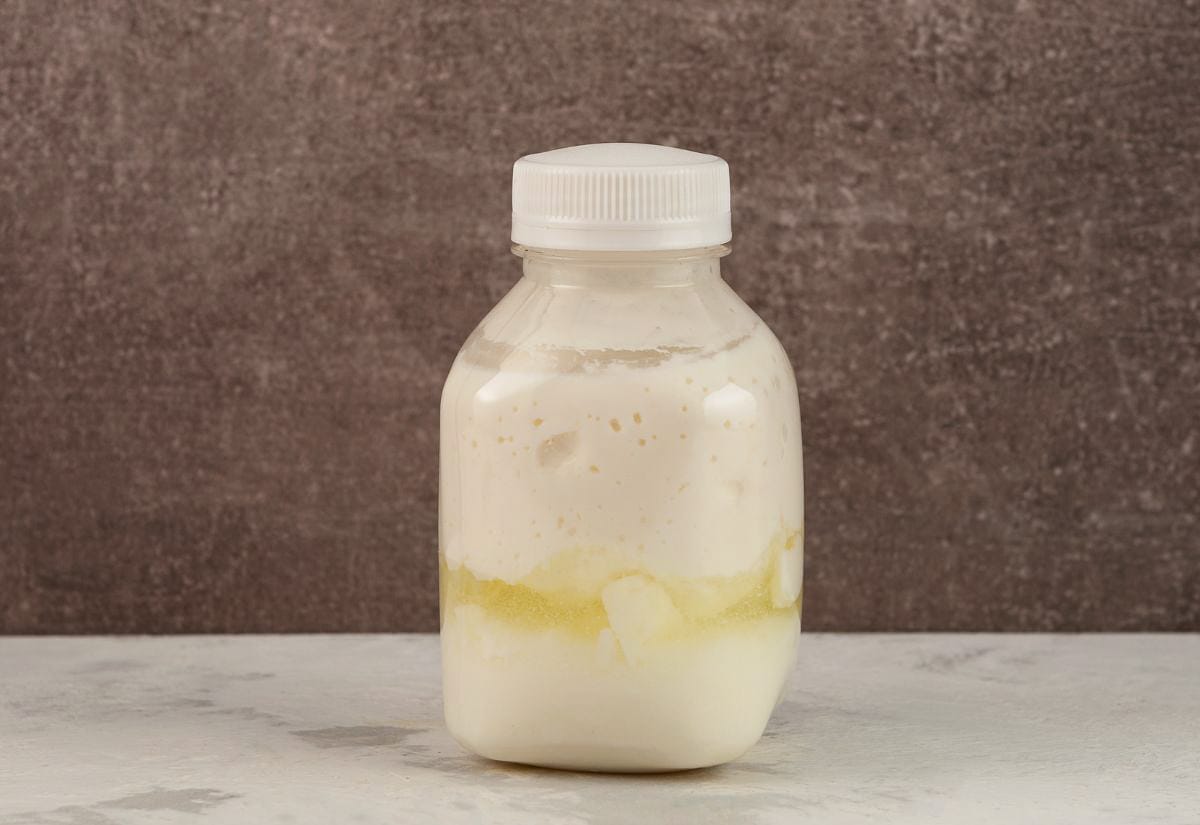 A clear plastic bottle filled with separated sour milk sitting on a light surface.
