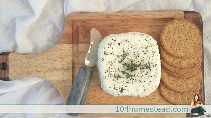 A cutting board with herbed chèvre and crackers.