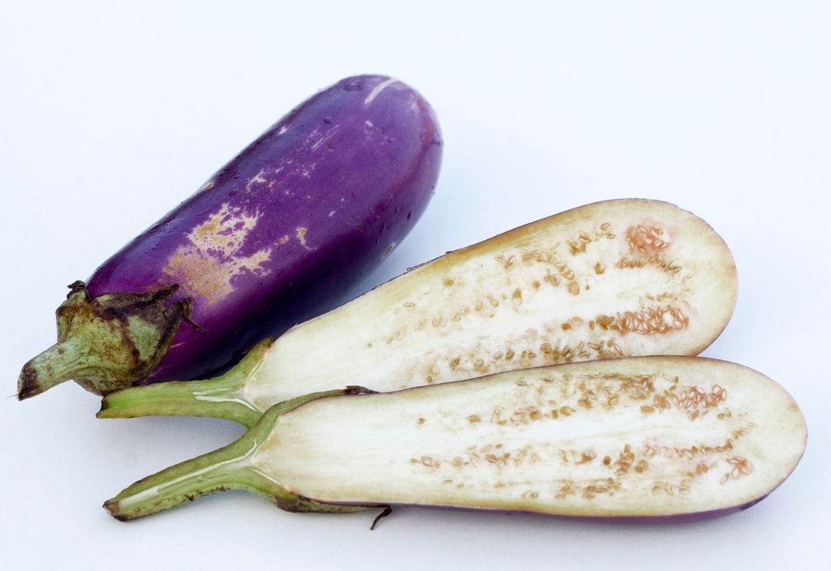 Whole eggplant next to a sliced eggplant, showing visible seeds inside.