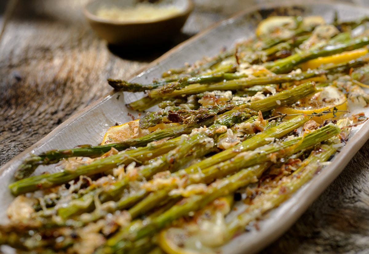 Grilled asparagus spears topped with lemon slices and melted cheese on a rustic platter.