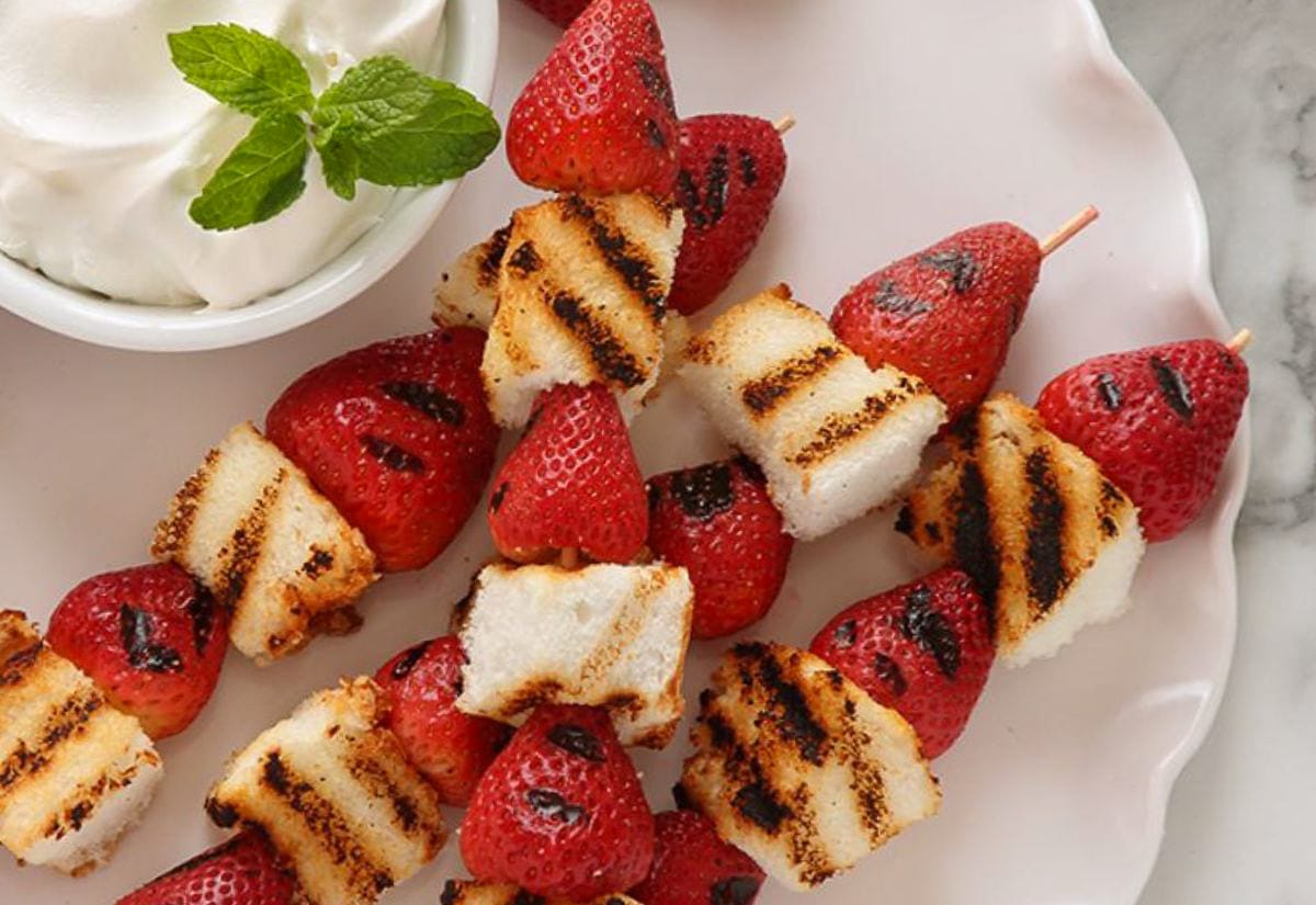 Grilled strawberry and angel food cake kabobs served with a bowl of whipped cream.