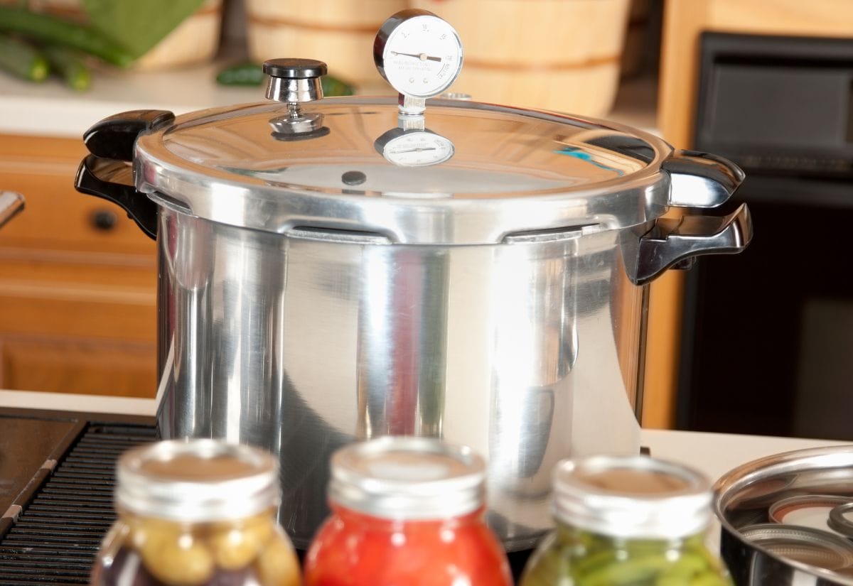 A stainless steel pressure canner with a gauge on a countertop, ready for preserving food safely.