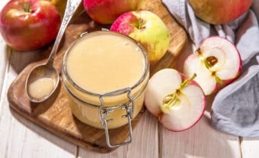 Close-up of a jar of homemade crockpot applesauce surrounded by fresh red and green apples.