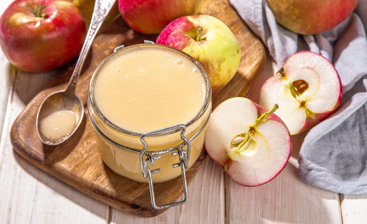 Close-up of a jar of homemade crockpot applesauce surrounded by fresh red and green apples.