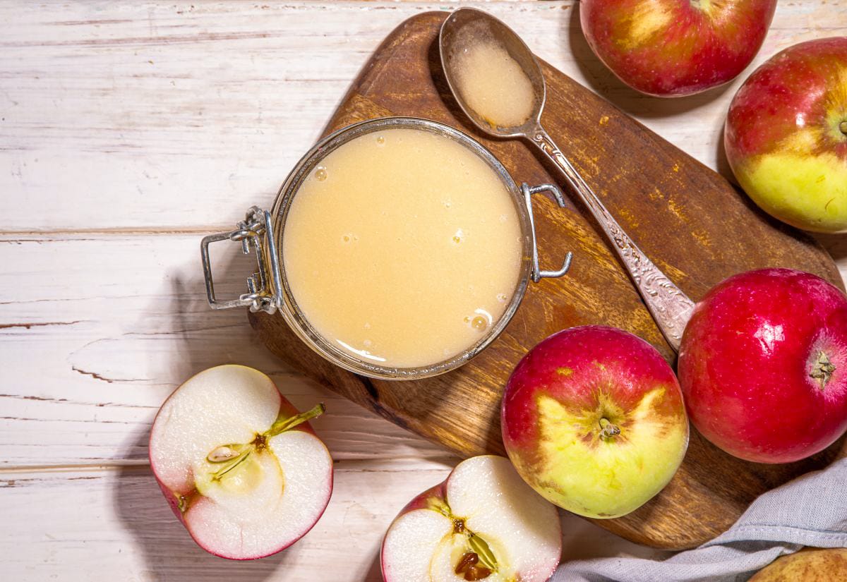Overhead view of a jar of crockpot applesauce on a wooden board with apples and a spoon.