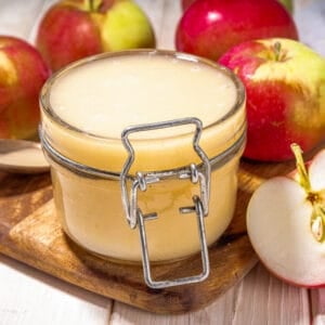 Close-up of a jar of homemade crockpot applesauce surrounded by fresh red and green apples.
