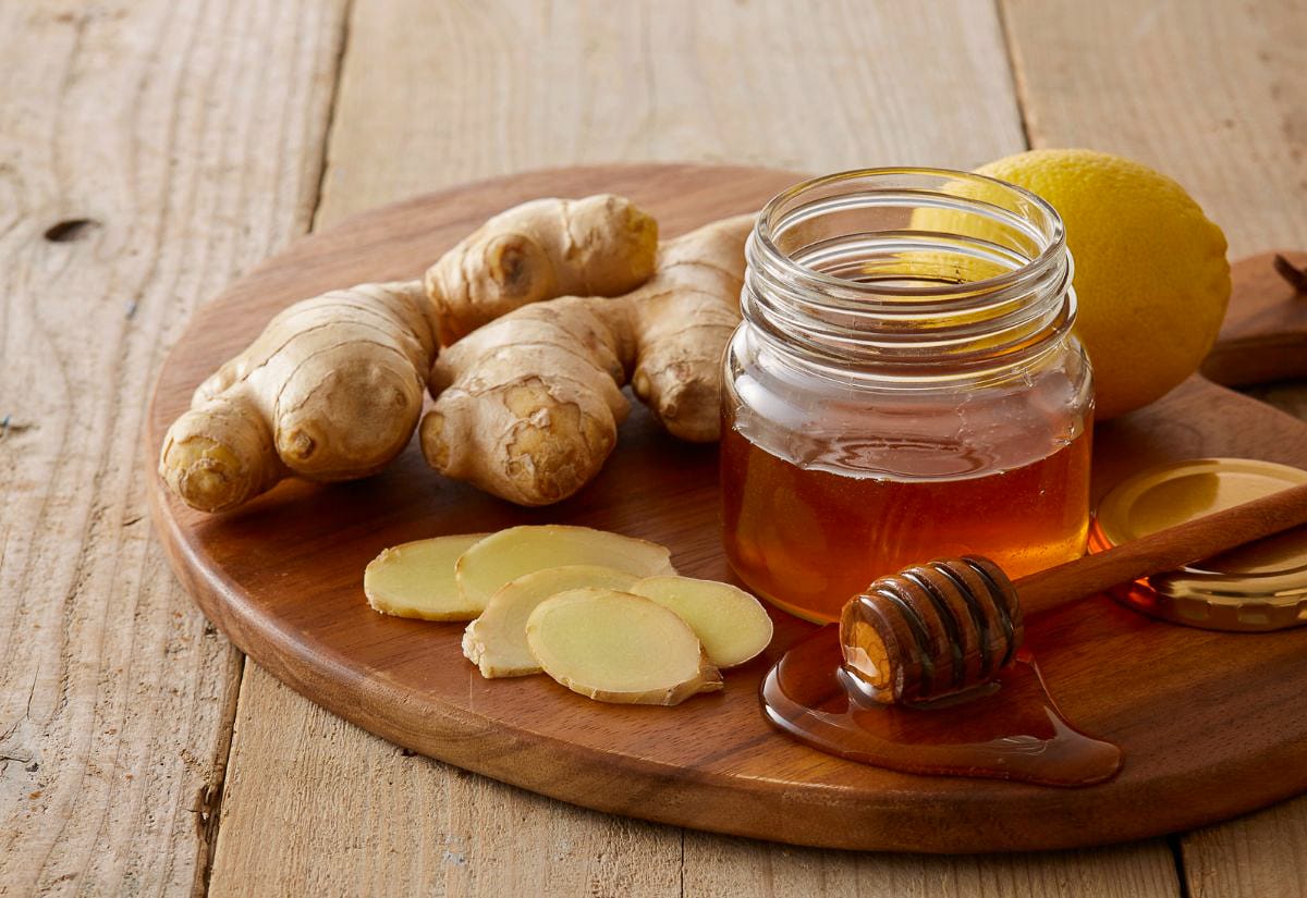 Fresh fire cider ingredients—ginger, turmeric, horseradish, garlic, onion, hot peppers, and a jar of honey—arranged on a wooden cutting board in a home kitchen.