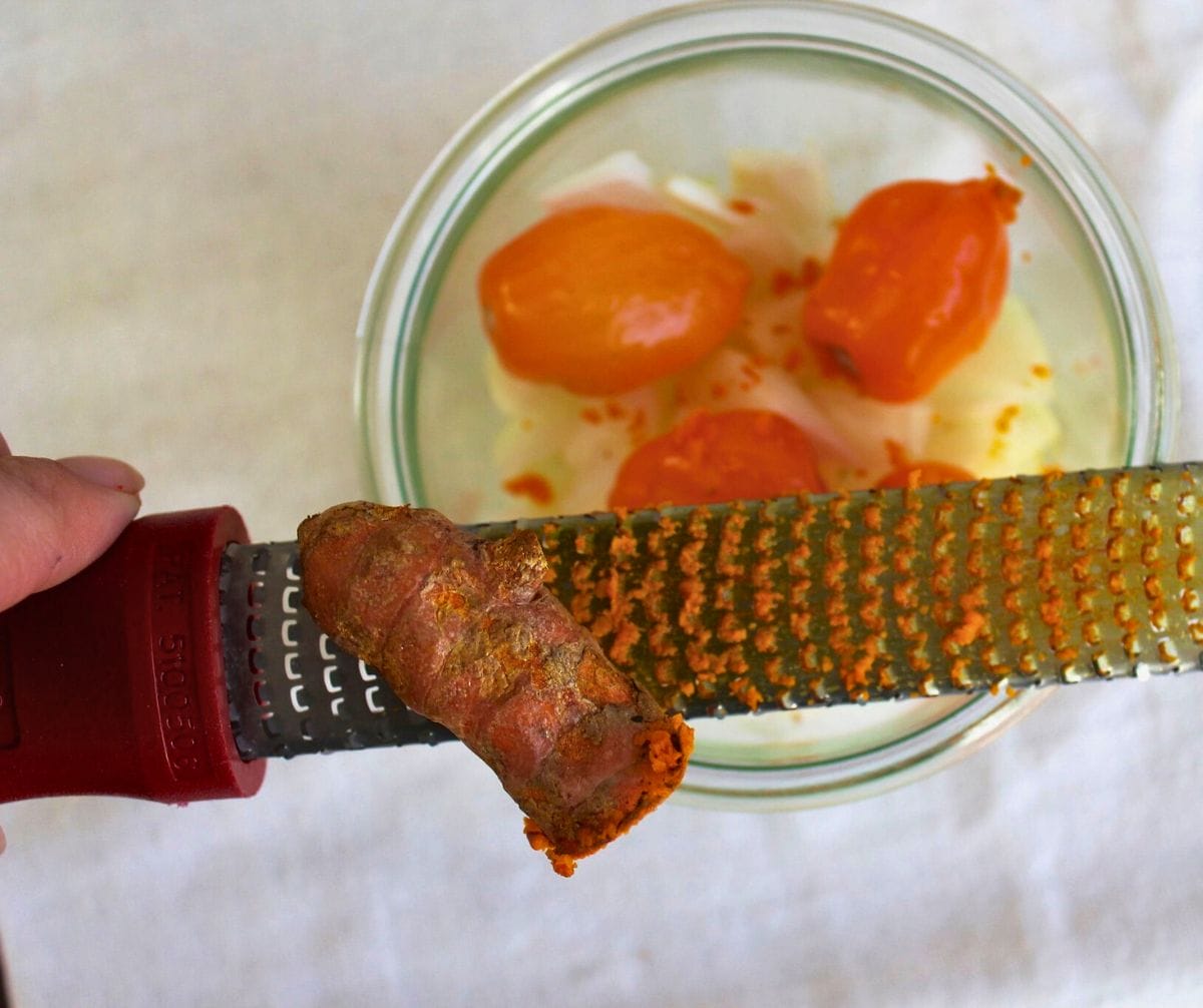 Grating turmeric root into a glass jar.