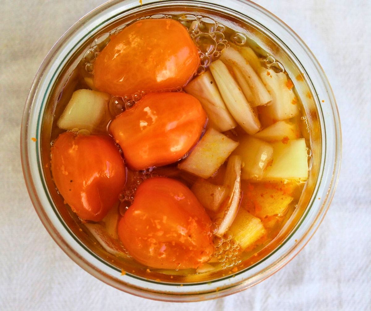 A glass jar of fire cider ingredients topped off with apple cider vinegar.