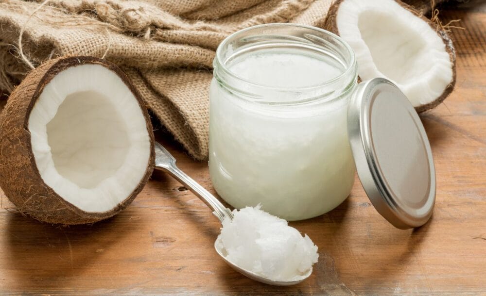 A cracked open coconut with a jar of coconut oil and a spoon.