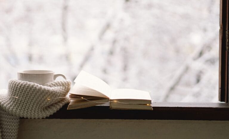 Open book and cozy mug on a windowsill with a snowy background.