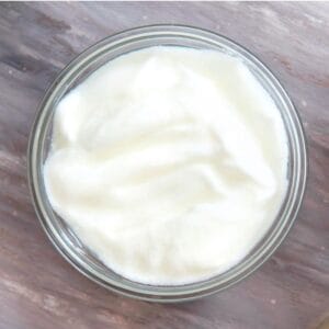 A glass bowl filled with smooth, creamy plain yogurt sitting on a textured gray background.