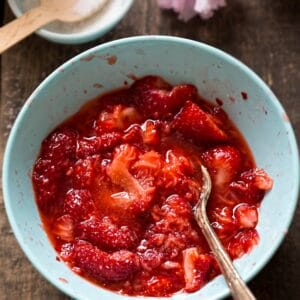 A light blue bowl filled with freshly mashed strawberries, with a vintage spoon resting inside, placed on a rustic wooden surface.