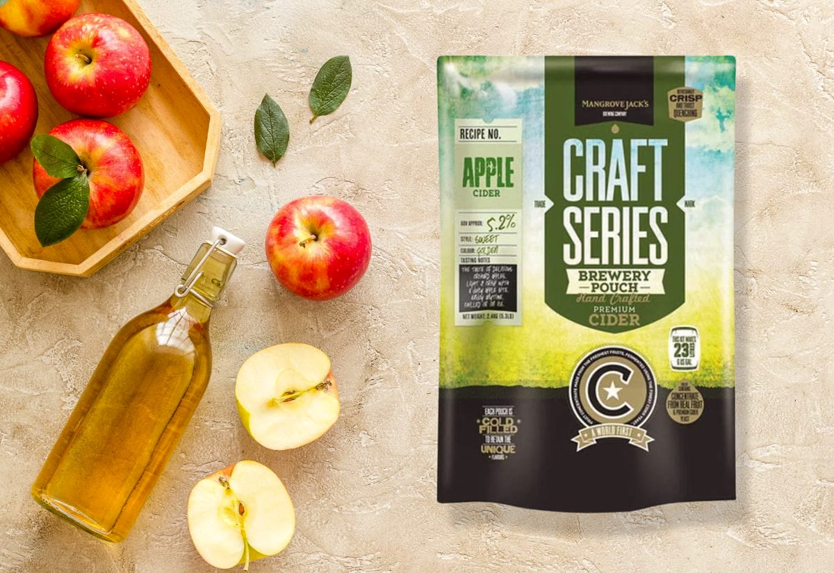 Fresh apples and a bottle of cider next to a Mangrove Jack’s Craft Series cider brewing pouch on a light stone background.