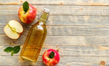 A bottle of hard apple cider on a wooden table with apples around it.