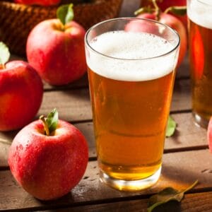 A glass of hard apple cider on a wooden table surrounded by fresh apples.