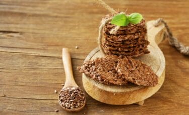 Flax seed crackers arranged on a wooden plate with a wooden spoon full of flax seeds.