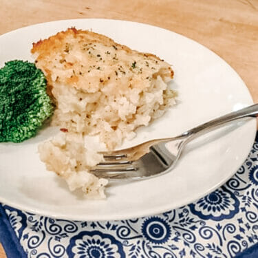 A portion of cheesy broccoli rice casserole on a white plate with broccoli florets.