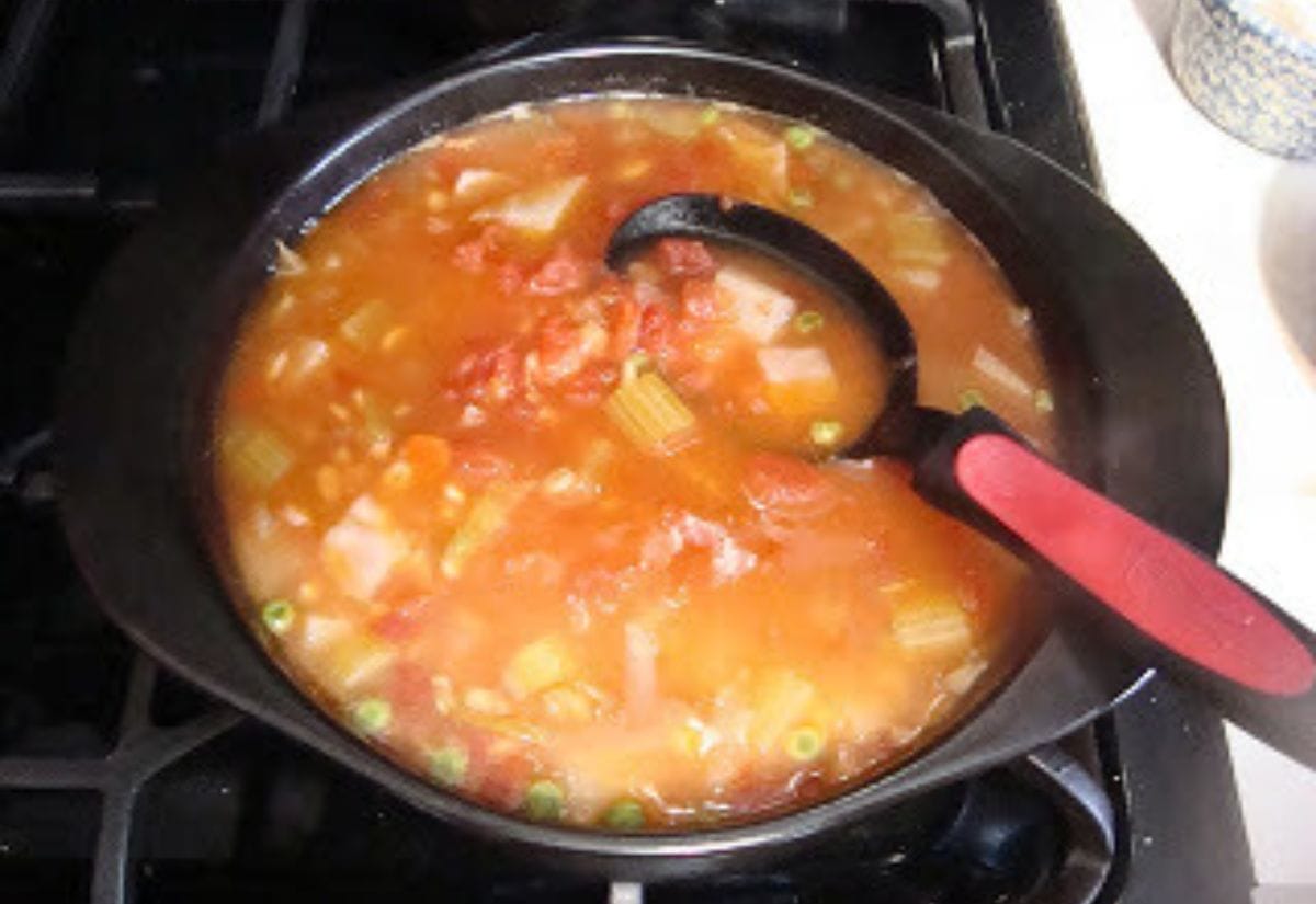 A simmering pot of vegetable barley soup filled with tomatoes, celery, peas, and carrots, with a ladle resting inside the pot.