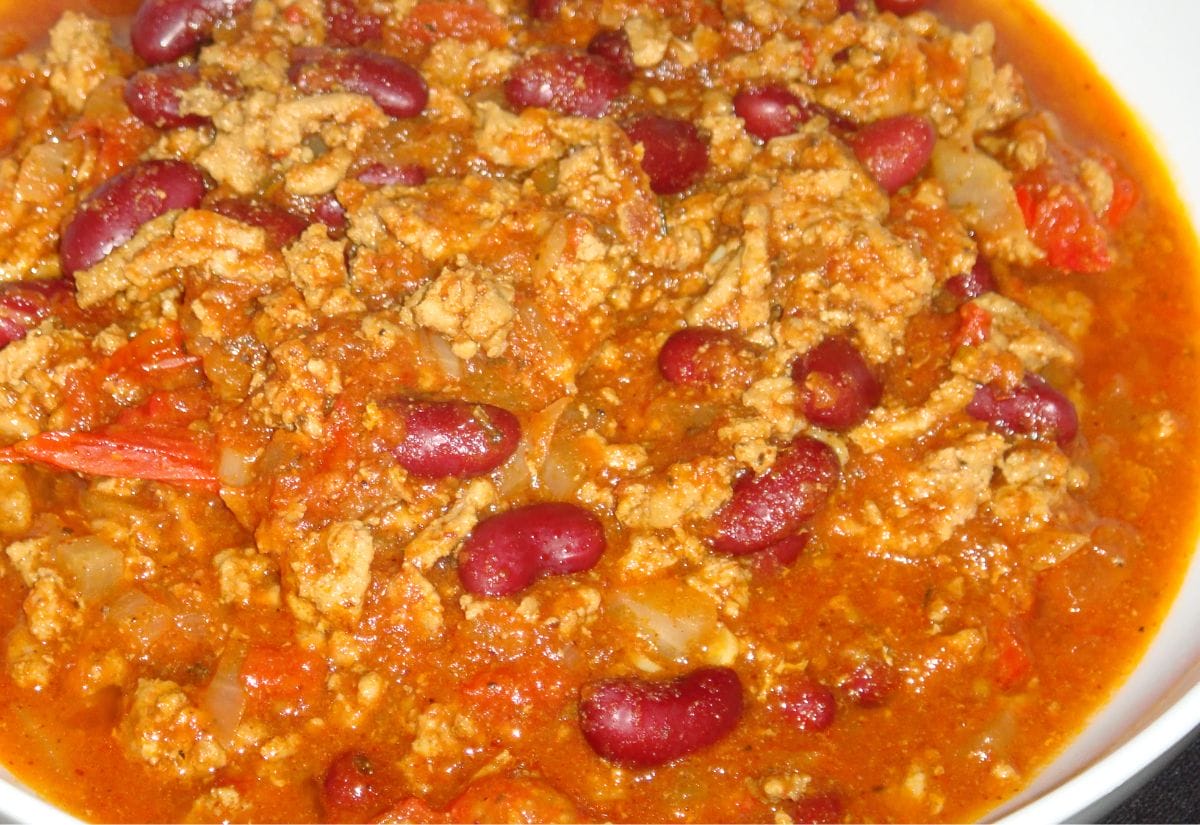 A close-up of hearty chili with red kidney beans, ground meat, and a thick tomato-based sauce, served in a white bowl.