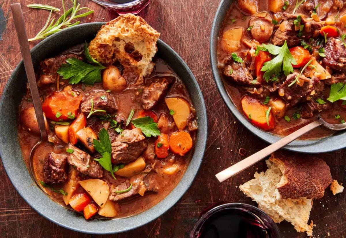 Two bowls of slow cooker beef stew filled with tender chunks of beef, carrots, potatoes, and garnished with parsley, served with crusty bread.