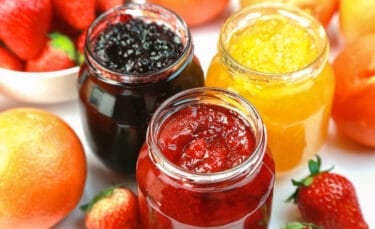 Three open jars of homemade jam—blackberry, strawberry, and peach—surrounded by fresh fruit. A visual of vibrant, no-sugar jam options.