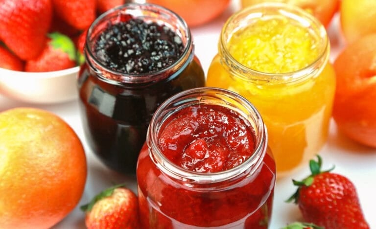 Three open jars of homemade jam—blackberry, strawberry, and peach—surrounded by fresh fruit. A visual of vibrant, no-sugar jam options.