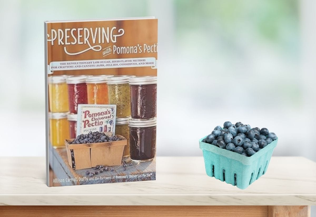 Pomona’s Pectin preserving book next to a basket of fresh blueberries on a bright counter.