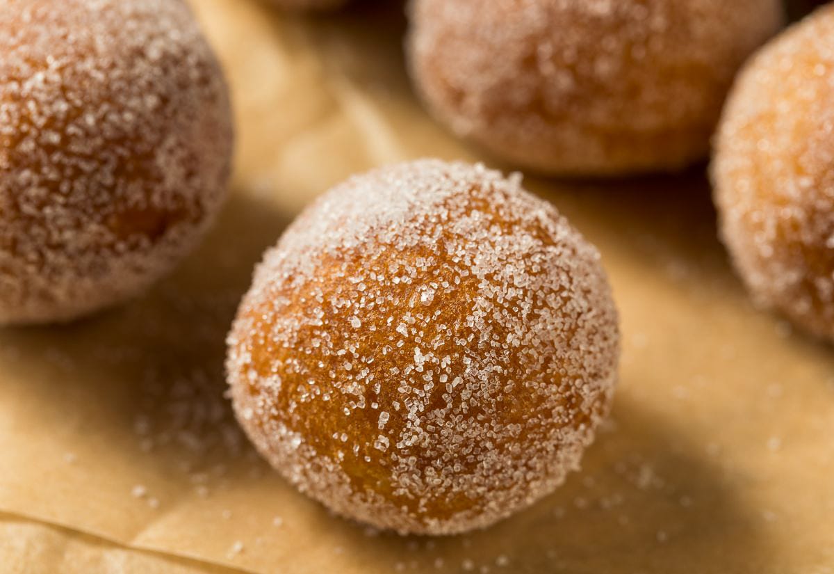 Close-up of a freshly fried sourdough donut hole coated in sparkling cinnamon sugar, showing the crisp golden crust and granulated texture.